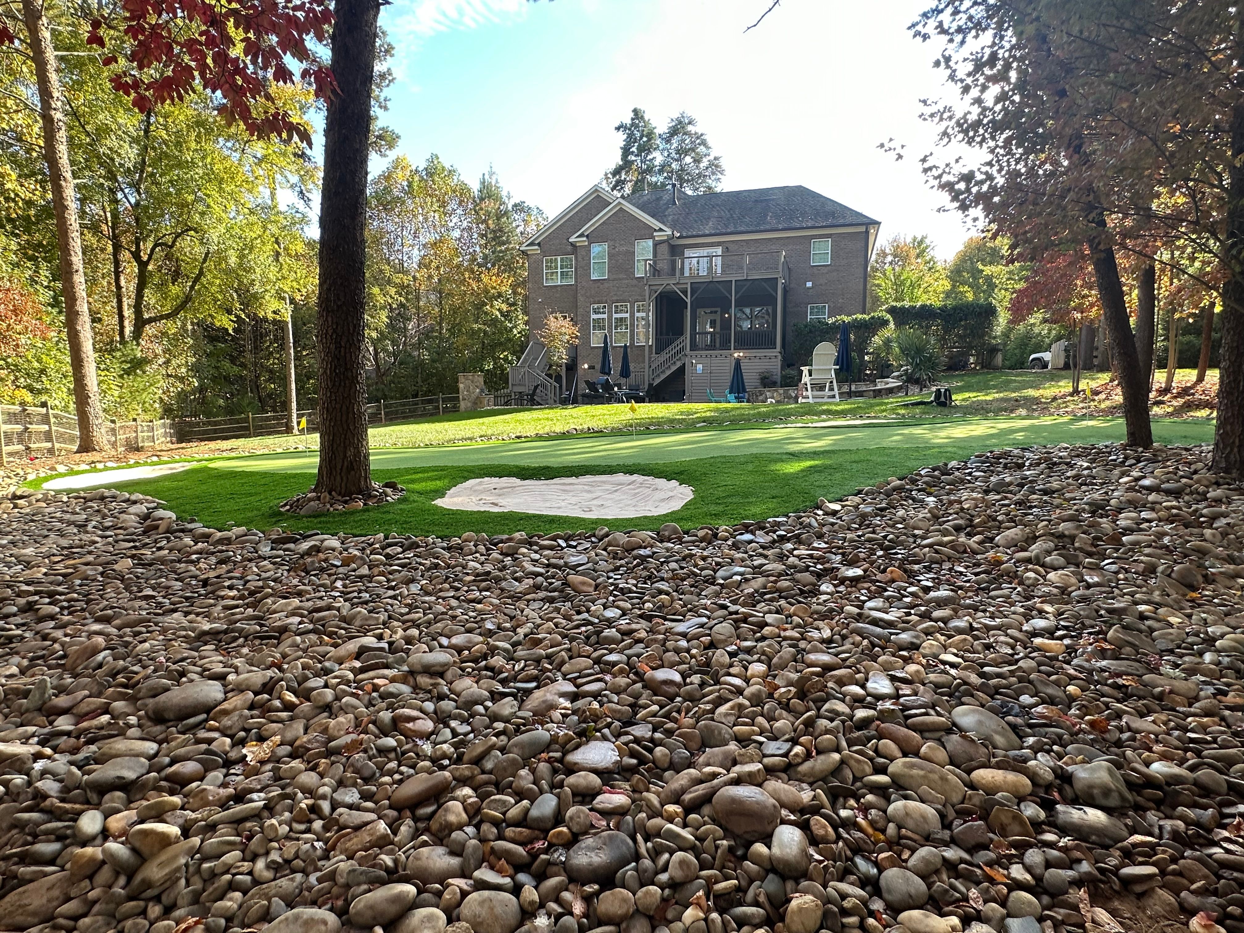 A professional-grade putting green in the backyard of a large home.